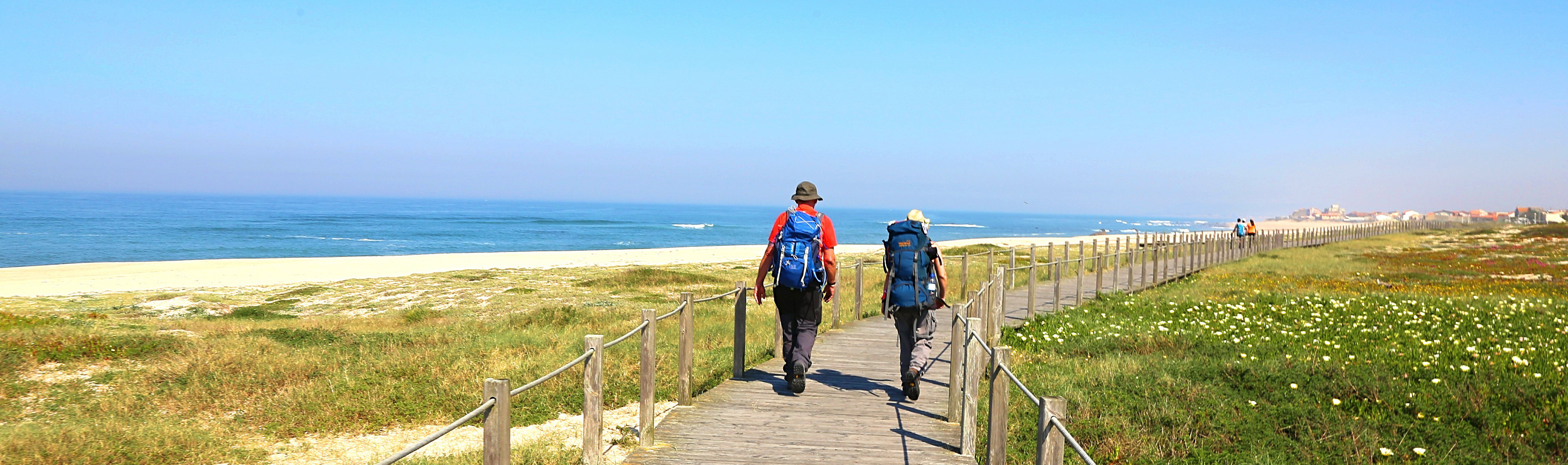 Two walkers on footpath along sandy coast with sea in the distance