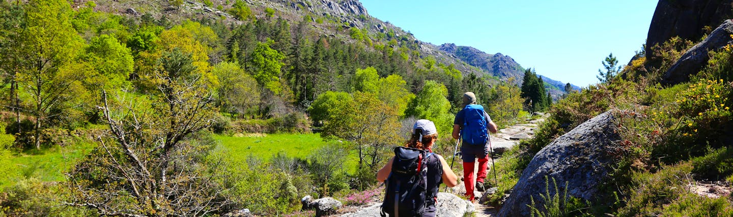 Two people in walking gear on a narrow stony path in hilly terrain