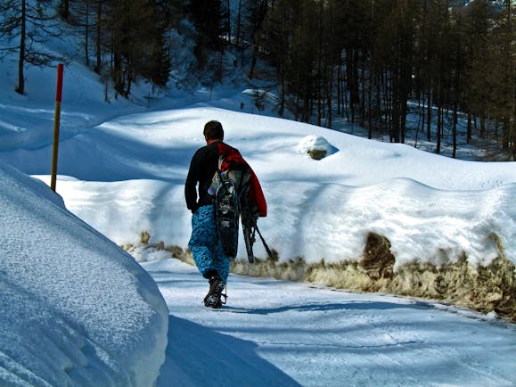 Man walking in winter on snowy track carrying snowshoes