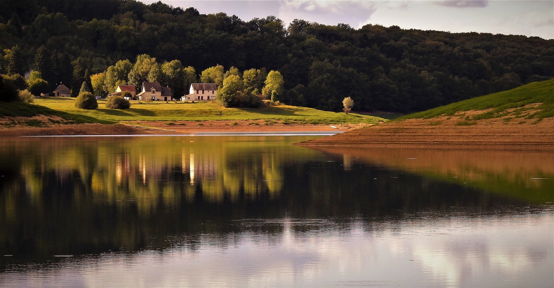 Lake in Burgundy with wooded hills and house in field behind