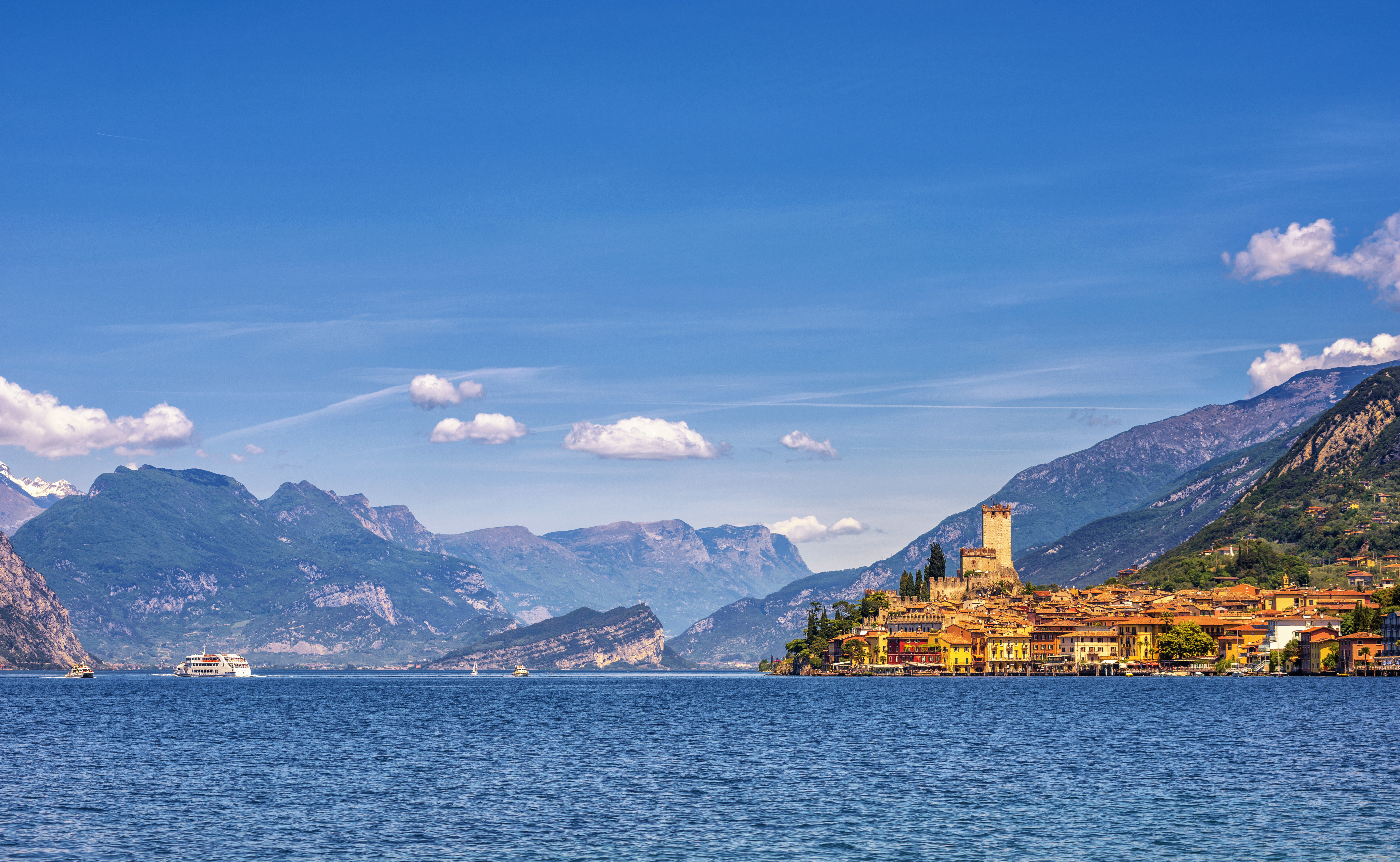 Orange coloured town of Malcesine perched on shore of blue waters of Lake garda with mountains