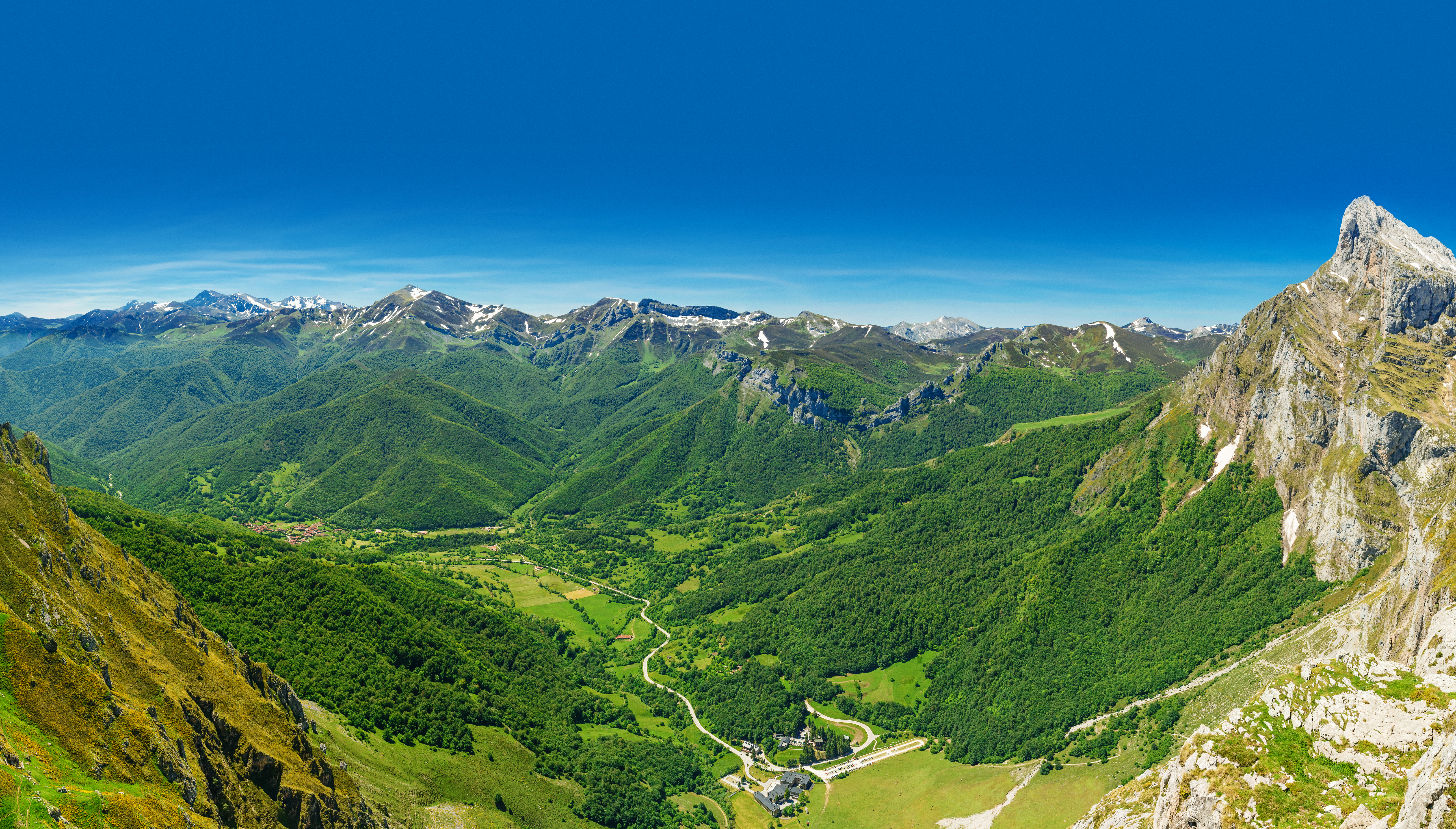 Wooded valley below mountains with snow on tops in the Picos de Europa in Cantabria