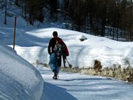 Man walking in winter on snowy track carrying snowshoes